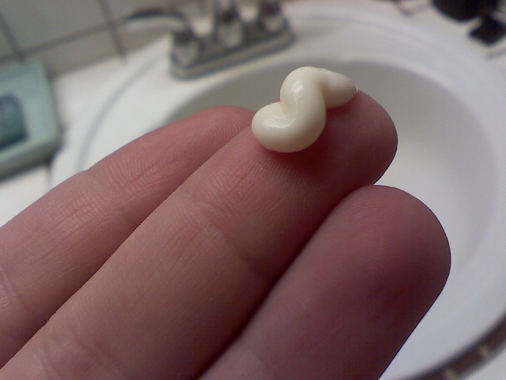 A dab of soothing aftershave balm on fingertips over a bathroom sink, ready to smooth onto a freshly shaved head