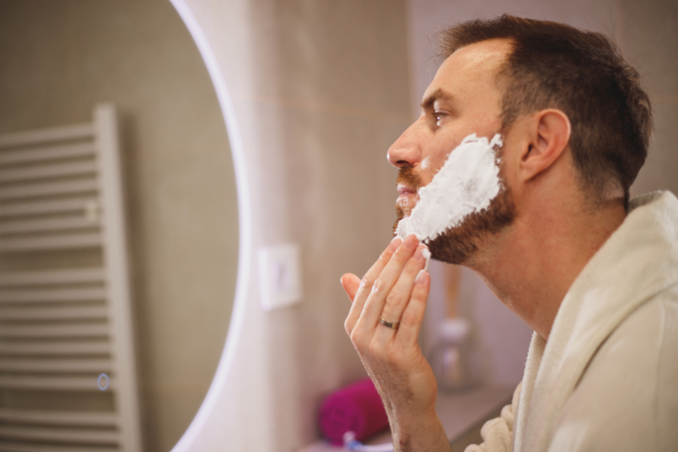 Man grooming and shaving at a bathroom mirror