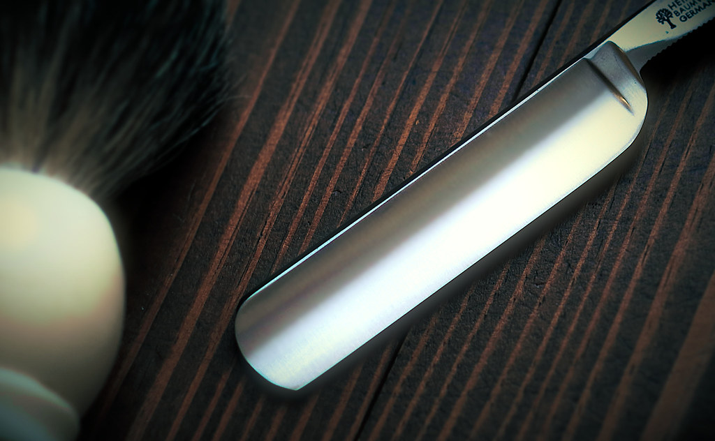 A straight razor and shaving brush laid on dark wood, the traditional kit for a straight-razor head shave