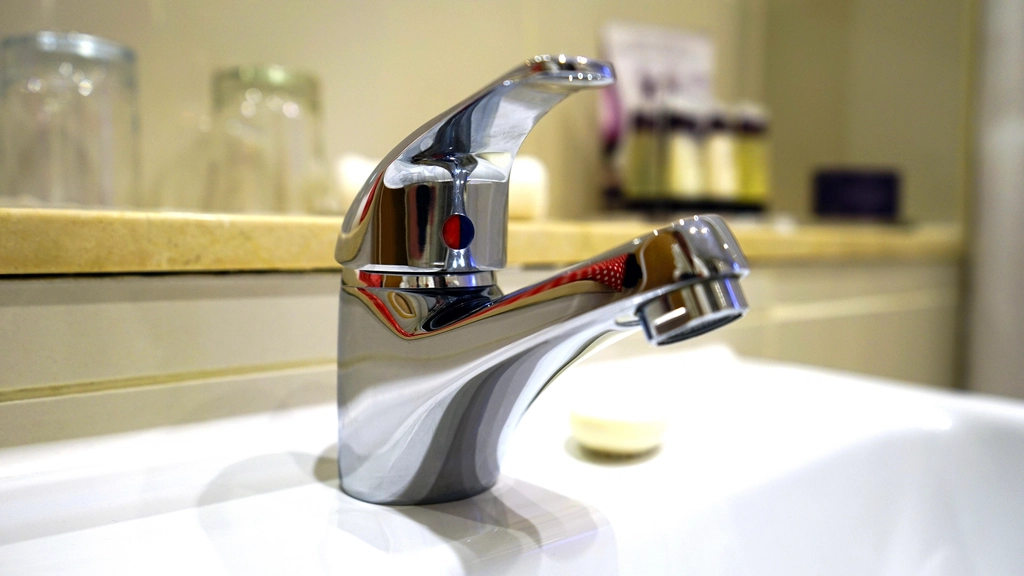 A clean chrome bathroom sink faucet, where a shaved head is rinsed and exfoliated