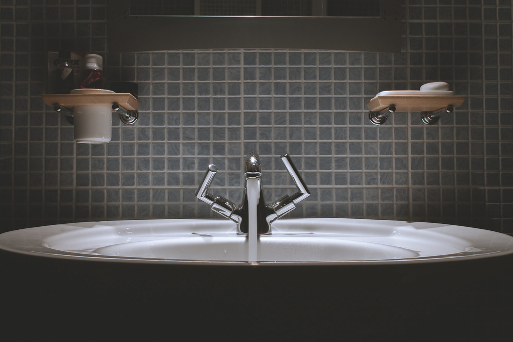 Chrome bathroom faucet running water into a sink, illustrating hard water and head shaving