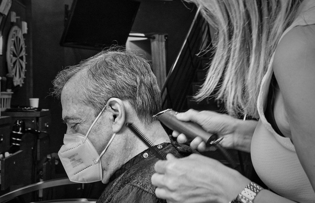 A barber using electric clippers to take a man's long hair down short before a head shave
