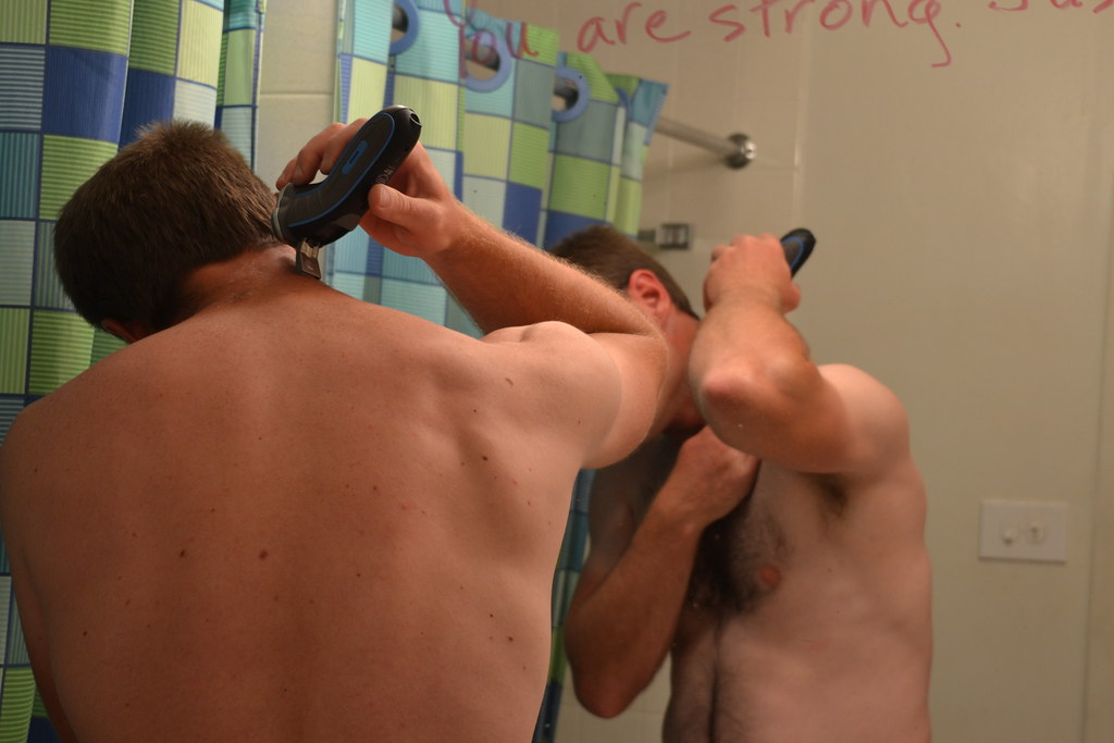 Man using an electric shaver on the back of his head and neck in the bathroom mirror